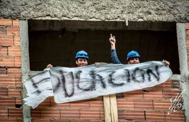 Trabajadores de obra con casco apoyando la defensa de la educación con un cartel desde piso alto de construcción